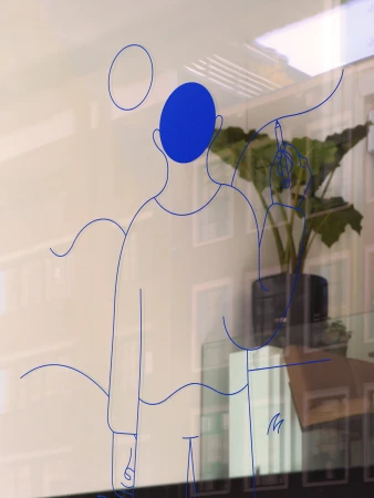 Line art on glass depicts a figure drawing on an interior window, with reflections of buildings and a potted plant visible.