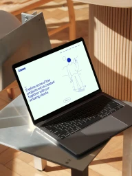 Laptop computer displaying brand website sitting on a metal chair in a brightly lit interior space