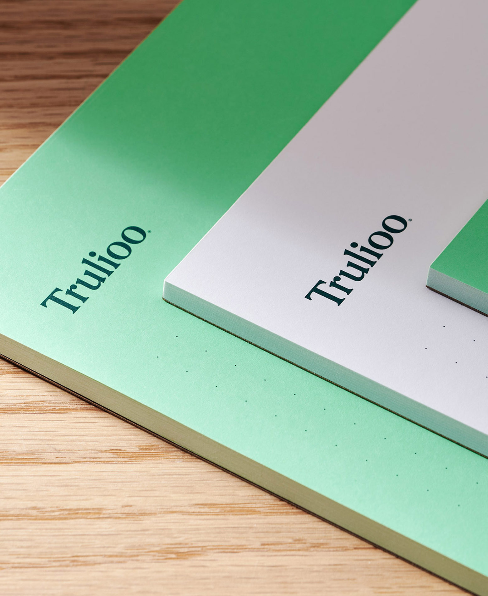 Close-up shot of green and white paper documents with the 'Trulioo' logo on a wooden surface, set indoors.
