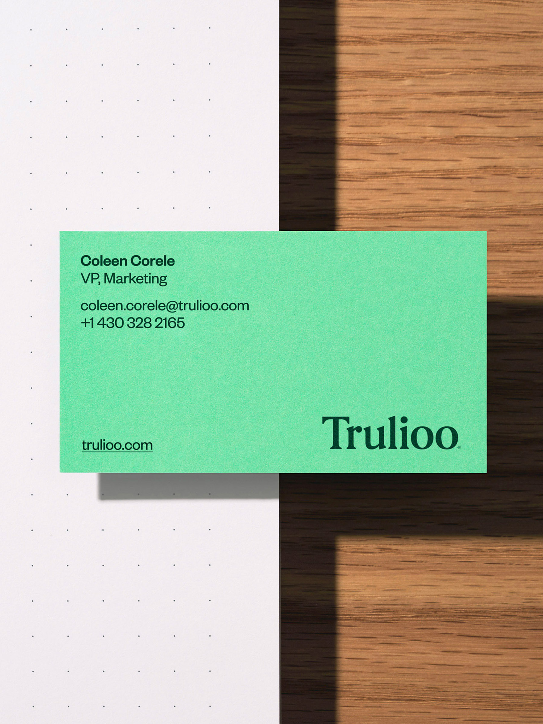 Close-up of a green business card with the company name Trulioo on a background split between white paper and a wood surface.
