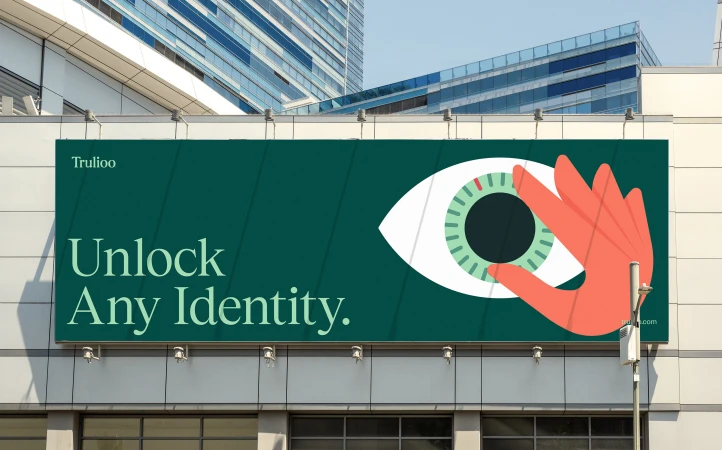 Billboard on a building features an eye graphic with a coral-colored hand unlocking it, next to the words 'Unlock Any Identity,' with Trulioo logo.