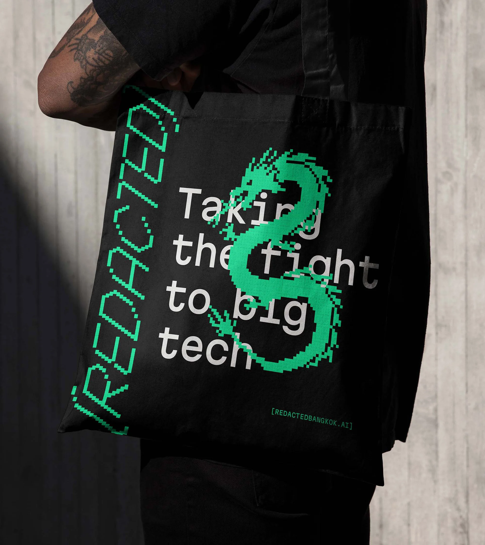 Tote bag held by a person, black with green dragon graphic and text, against a neutral background.