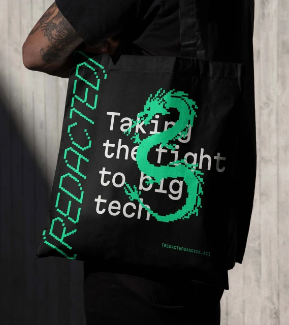 Tote bag held by a person, black with green dragon graphic and text, against a neutral background.