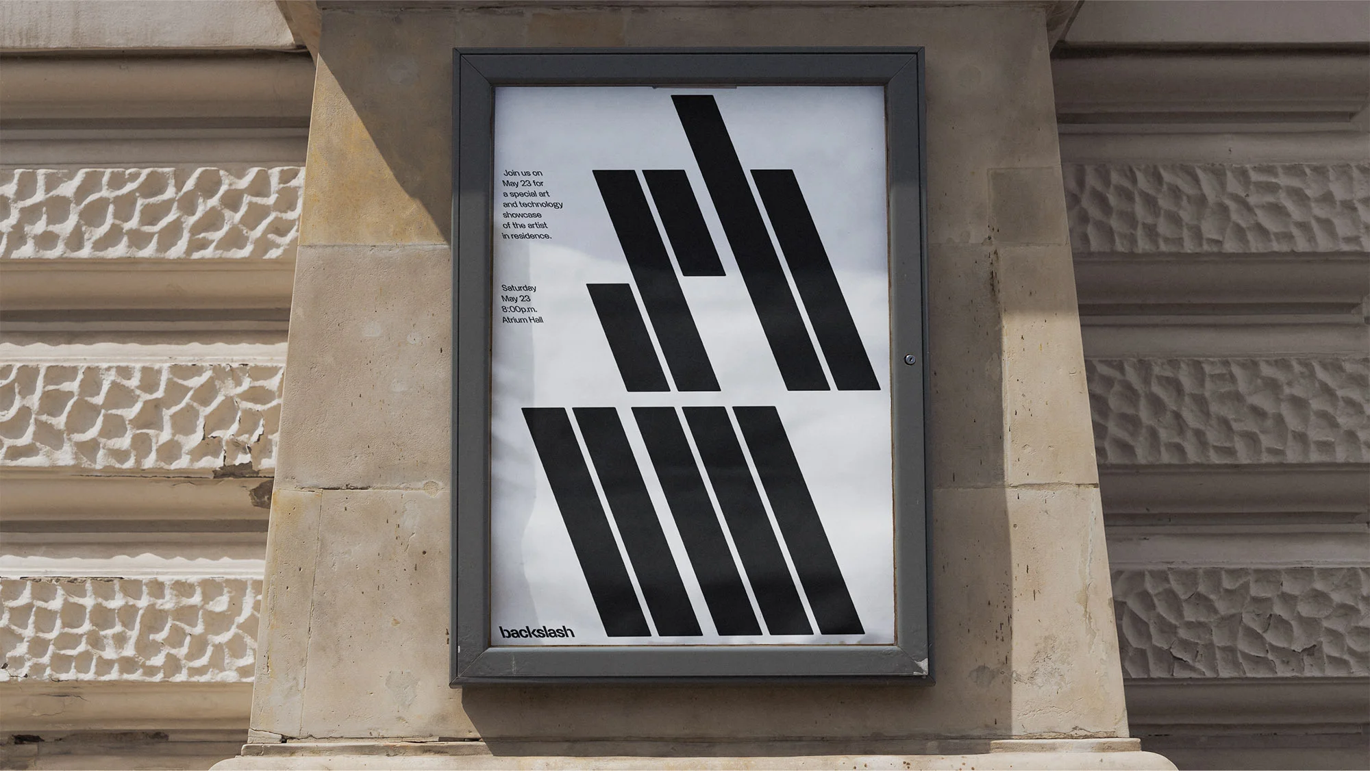 Poster in gray frame attached to a light stone wall with carved horizontal patterns. The poster has black abstract geometric design.