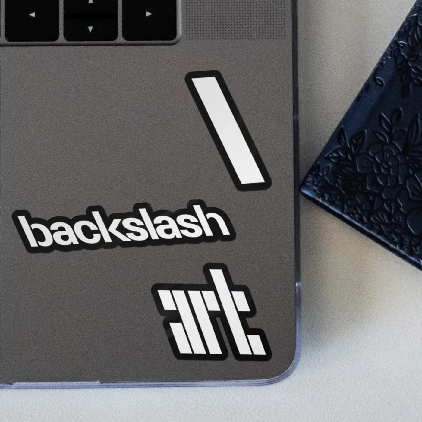 Close-up of a grey laptop lid decorated with white vinyl stickers displaying the backslash brand identity and typography.