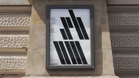 A dark framed poster featuring bold black geometric shapes on white paper displayed on an ornate stone building exterior wall