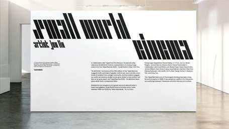 Large white exhibition wall with bold black diagonal stripe typography in a concrete gallery interior.