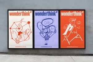 Three framed posters featuring colourful graphic illustrations and bold typography mounted on a concrete wall.