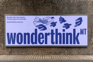 Large horizontal billboard featuring blue typographic branding and illustrations of a figure and birds mounted on a dark brick wall
