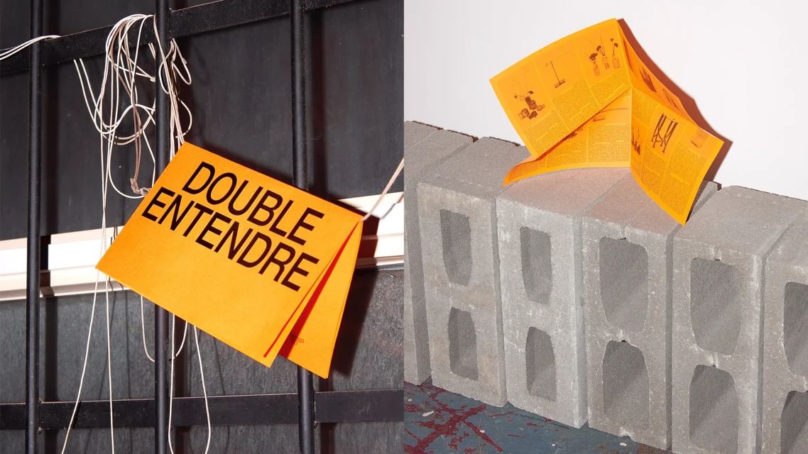 Two orange signs: One hanging on a black barred window with the text “Double Entendre,” and another on gray concrete blocks.
