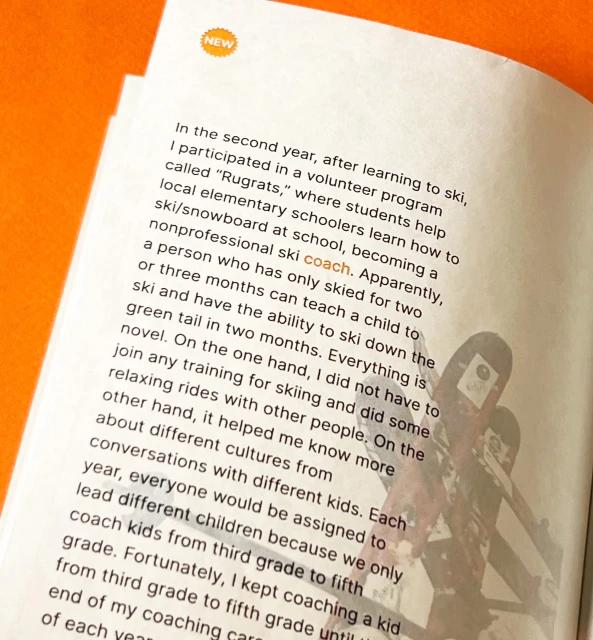 Open book with text about a ski coach program, featuring a partial image of ski equipment in the corner, against an orange surface.