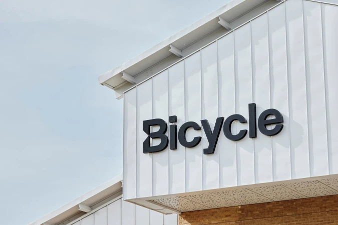 Architectural shot of a commercial building with a white facade and a large black 'Bicycle' sign, clear skies visible above the building.