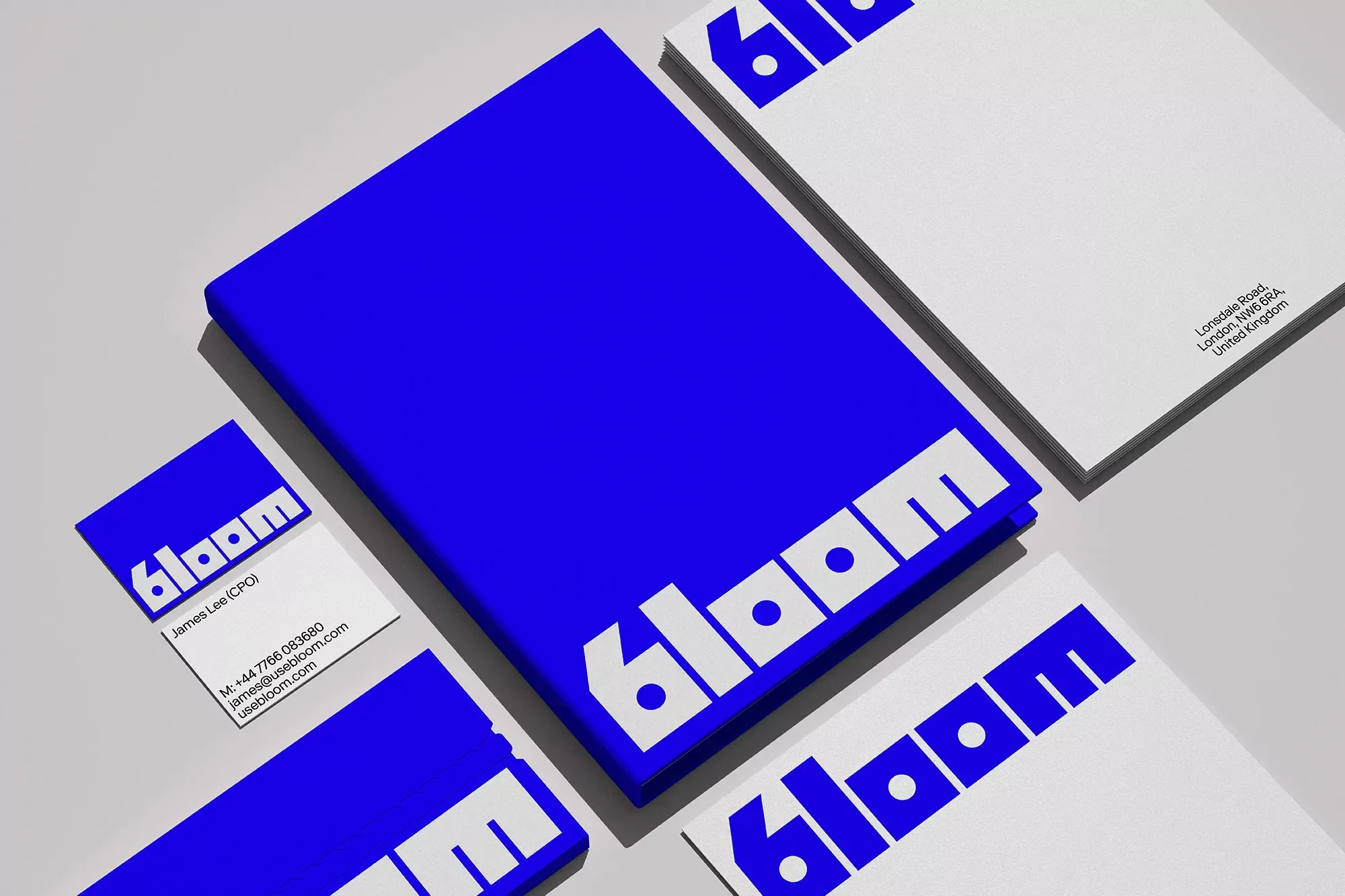 Stack of blue and white 'Bloom' branded stationery including letterhead, business cards, and a thick notepad on gray surface.