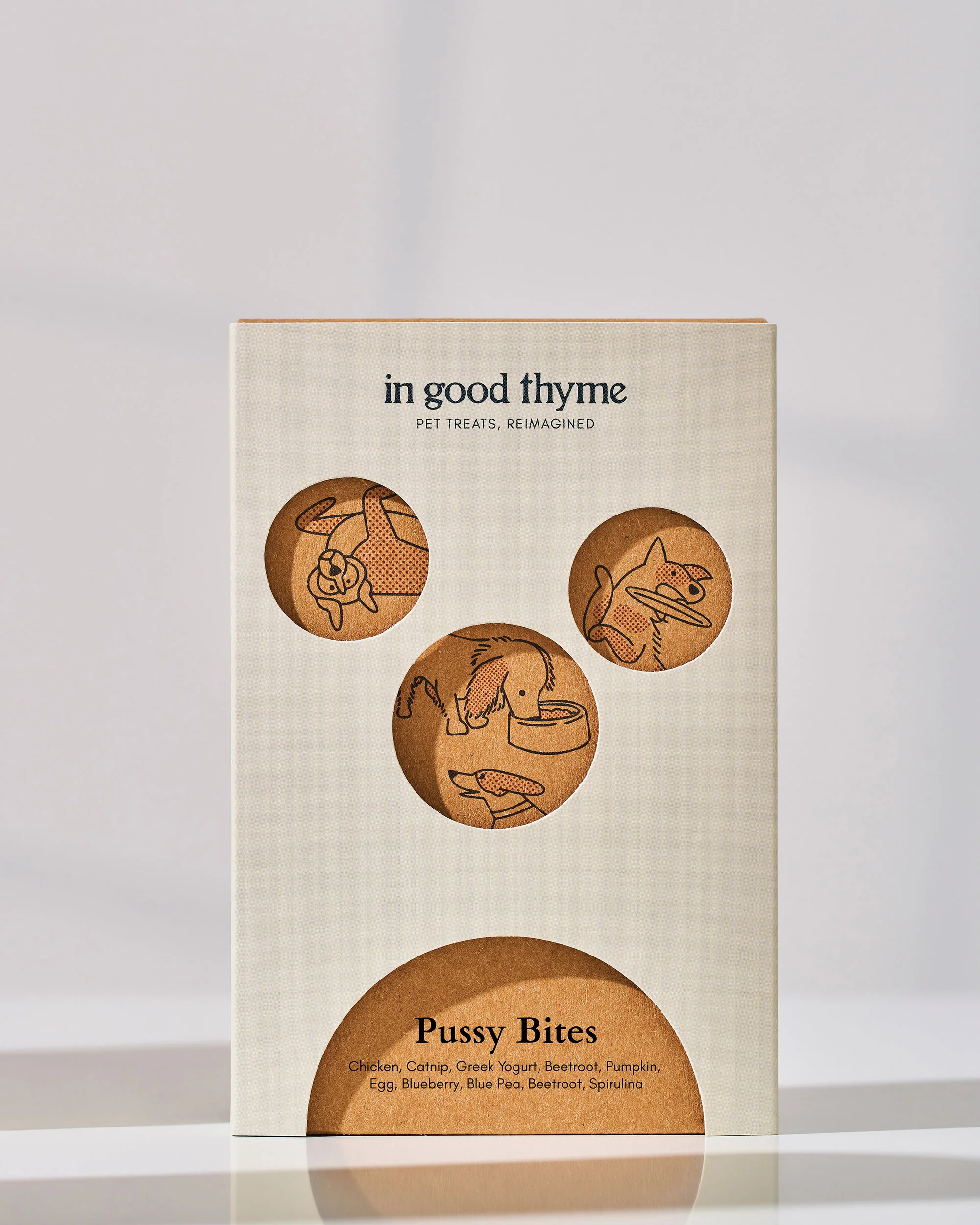 Tan box of In Good Thyme Pussy Bites cat and dog treats with animal illustrations against a white background and soft lighting.