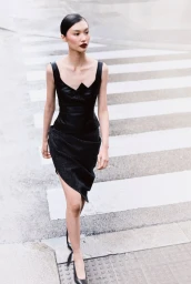 Asian woman walking across a pedestrian crosswalk wearing a black sleeveless top and dark skirt