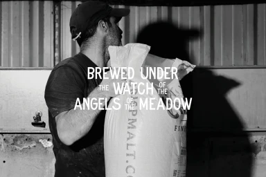 Man wearing a cap holding a large white sack inside a brewery with corrugated metal walls
