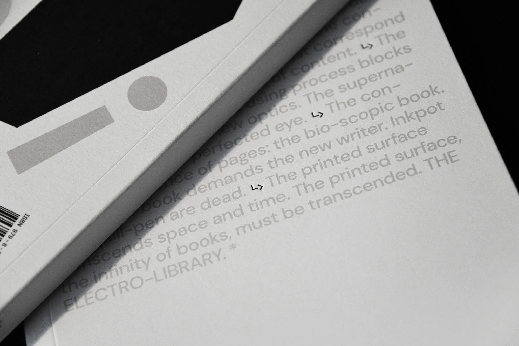 Close-up of a book cover and pages with grey, textured text on a white surface; the book has a spot varnish and a barcode.