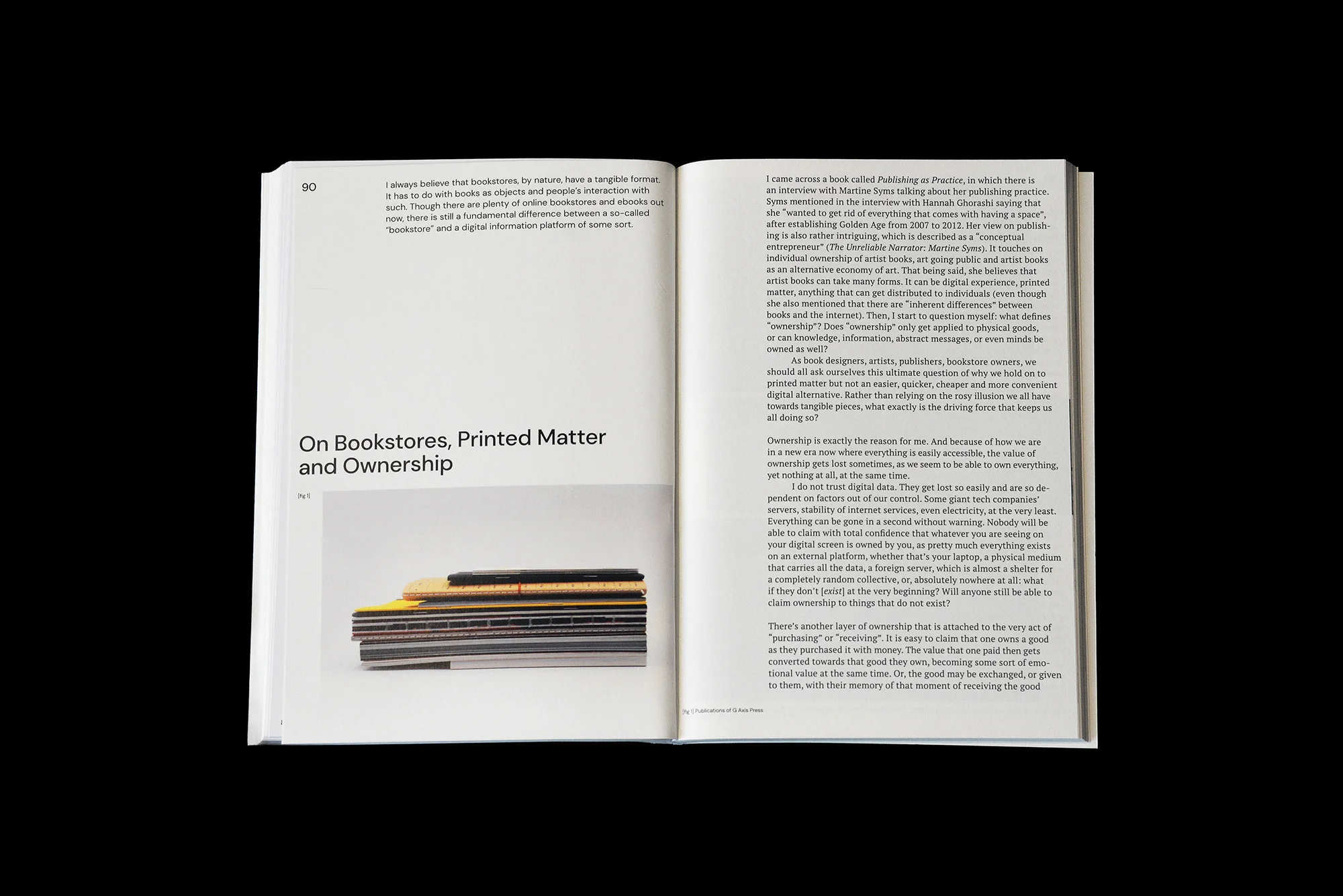Open book spread with text about bookstores, printed matter, and ownership, alongside a stack of books with colorful covers on a white surface.
