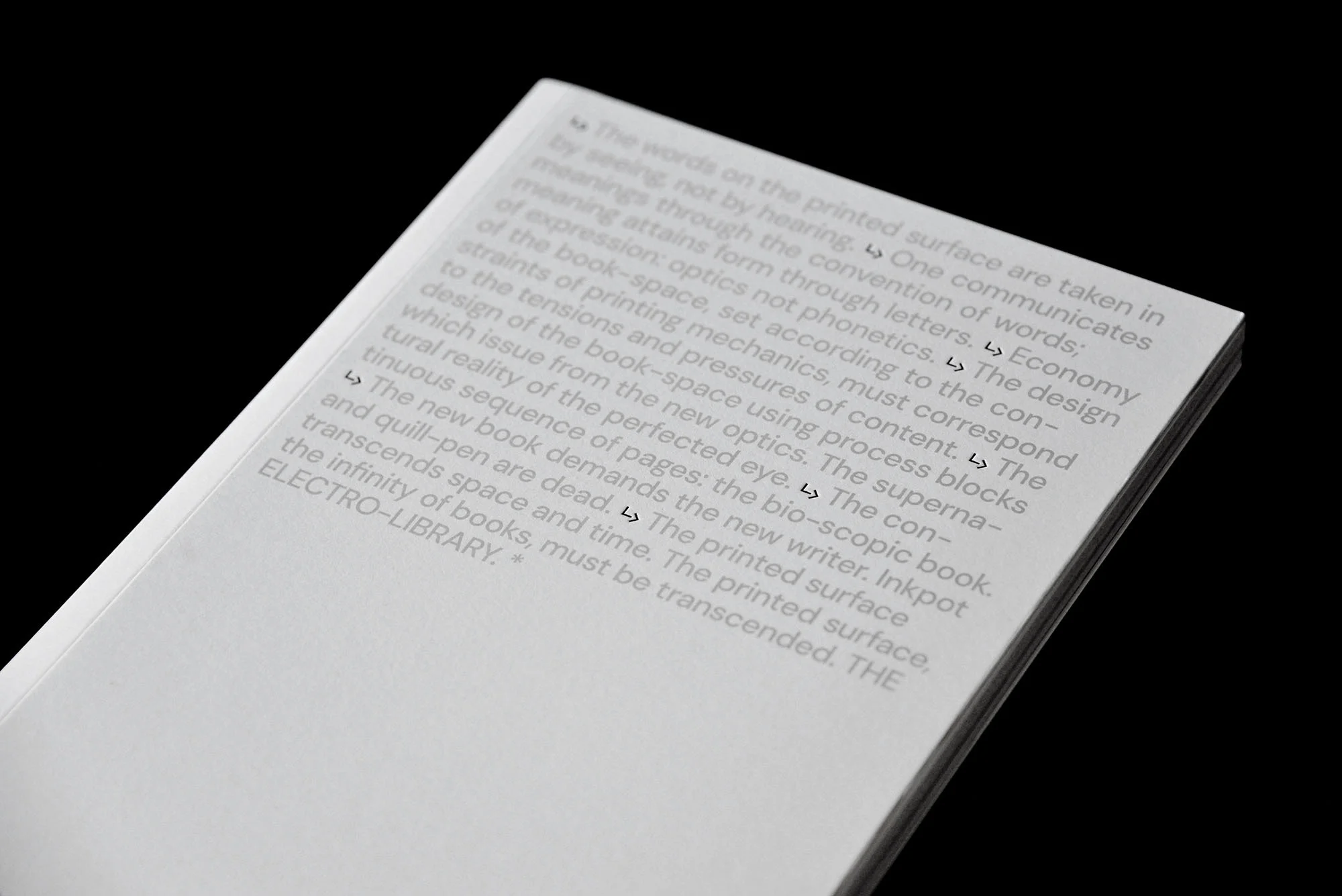 Open book showing pages of text in the English language against a black background. The book is white, and the text is grey.