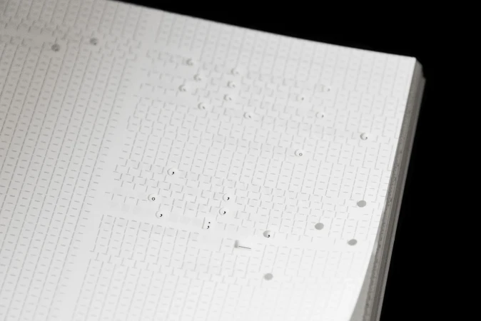 Close-up of a white paper notebook featuring debossed typographic grid patterns and delicate punctuation marks