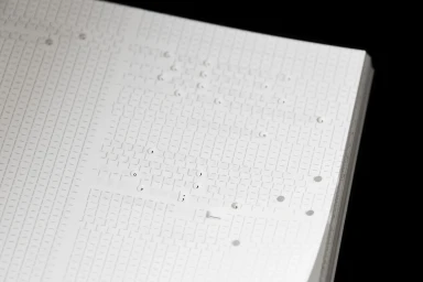 Close-up of a white paper notebook featuring debossed typographic grid patterns and delicate punctuation marks