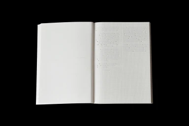 An open notebook with grid paper and embossed dots on the right page against a black background.