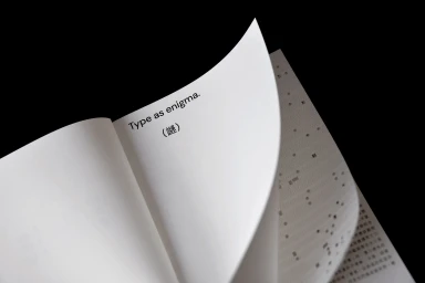 Close-up of turning pages in a white book featuring printed typography against a solid black background.