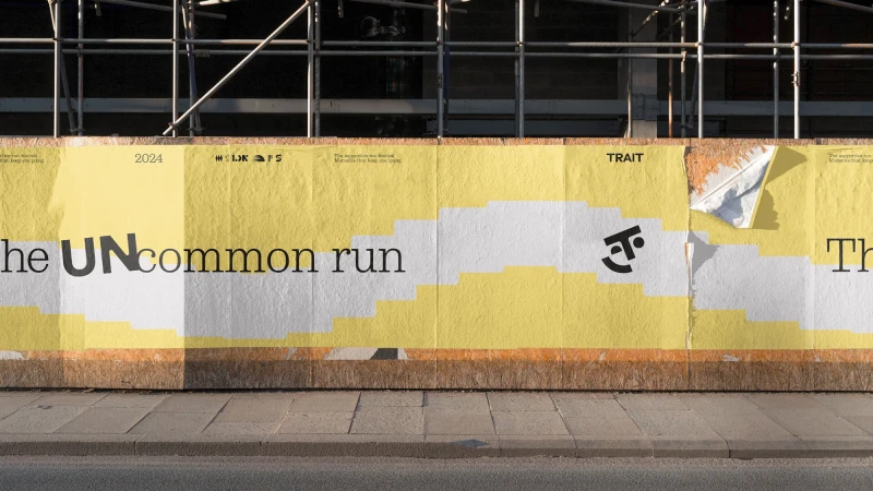 Outdoor advertising billboard featuring 'The Uncommon Run' event with a playful logo, set against a city sidewalk and scaffolding.