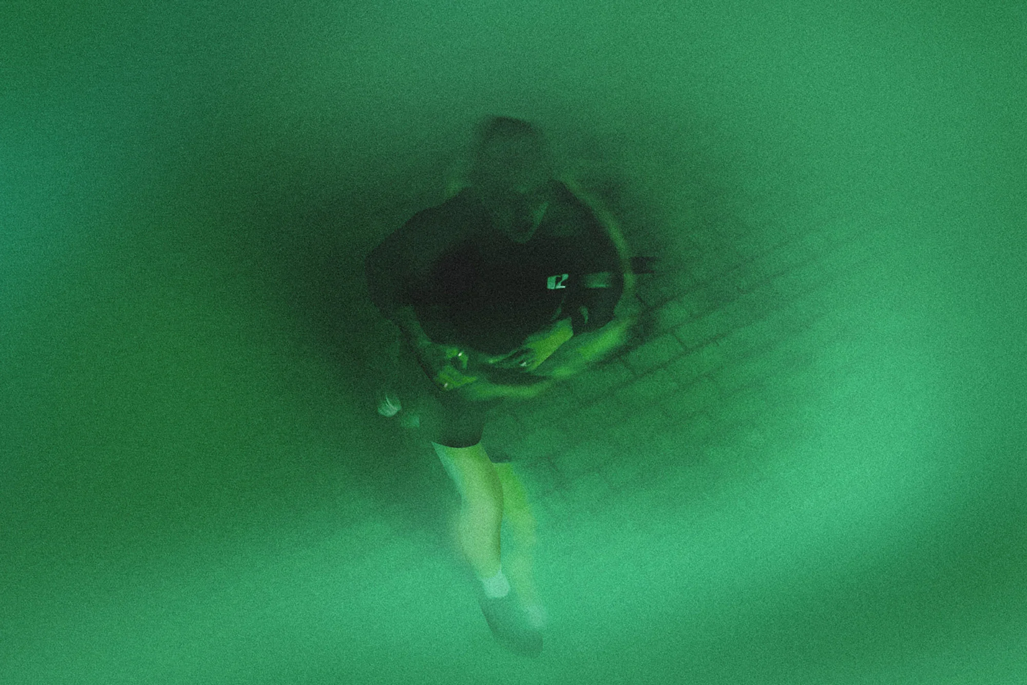 Underwater diver in a dark wetsuit and fins, swimming in blurry green water with a net and diffused light. Underwater scene.