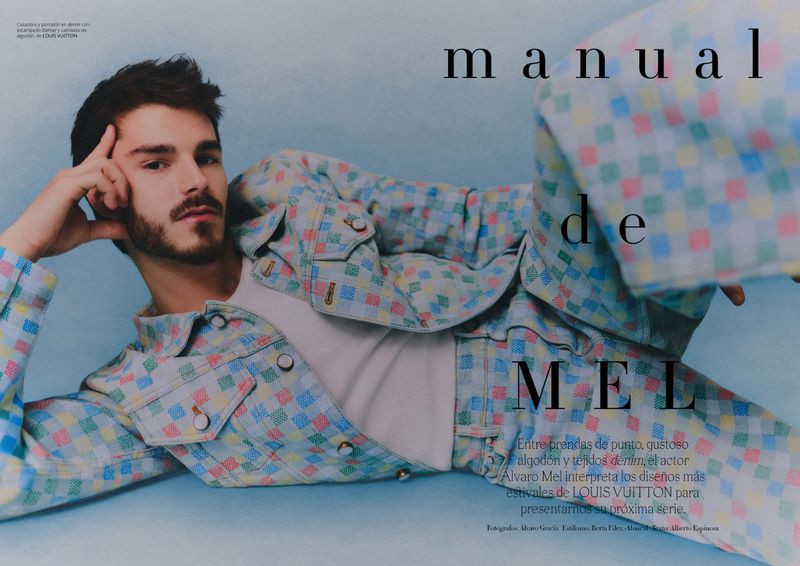 Alvaro Mel poses in a pastel checkered jacket and pants. He is laying down against a light blue background and holding his head with one hand.