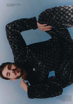 Man wearing a black patterned tracksuit posing dynamically against a solid blue background for an editorial spread.