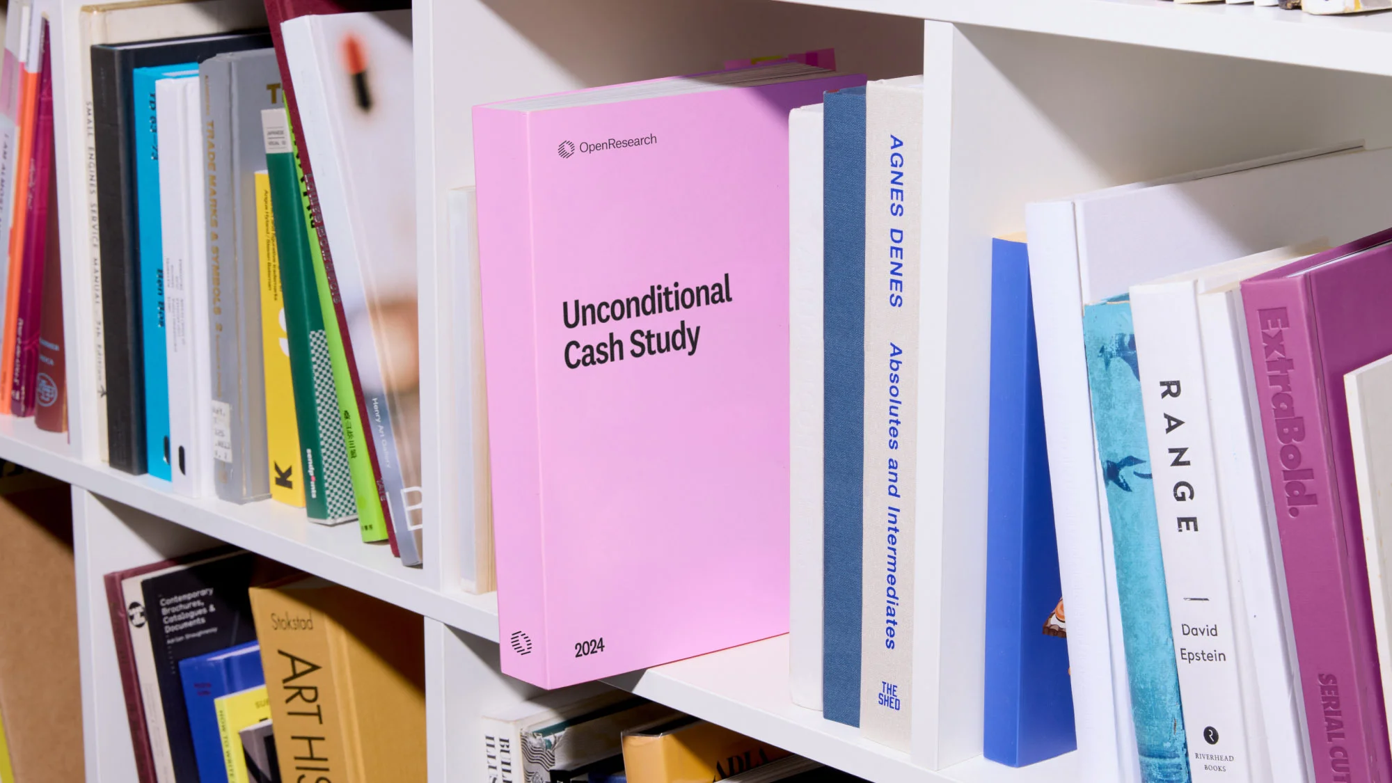Image of a bookshelf filled with various books, including one pink book titled "Unconditional Cash Study" by OpenResearch.