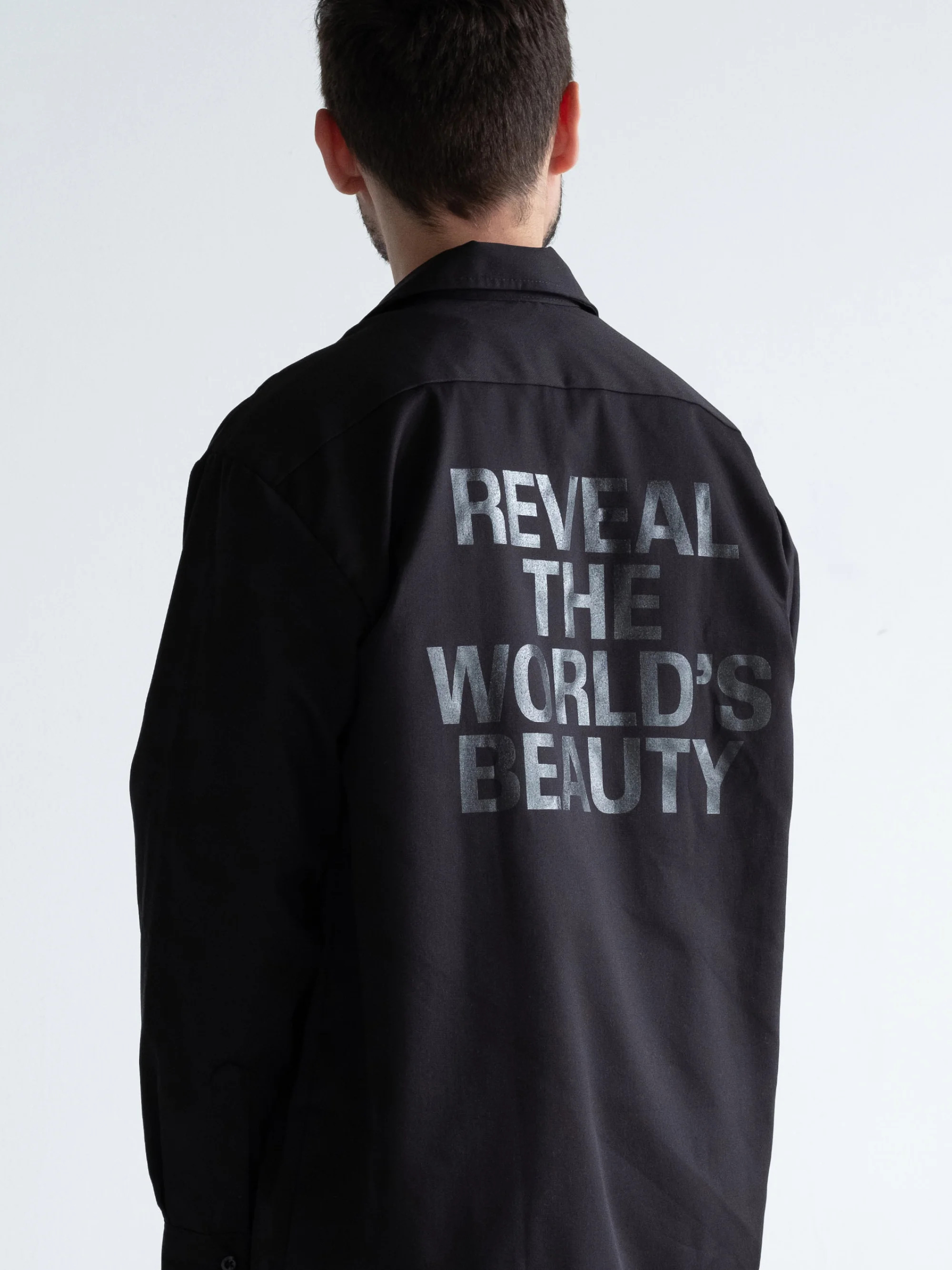 Man wearing a black shirt with text printed on the back against a plain white background for L'Eloi brand identity
