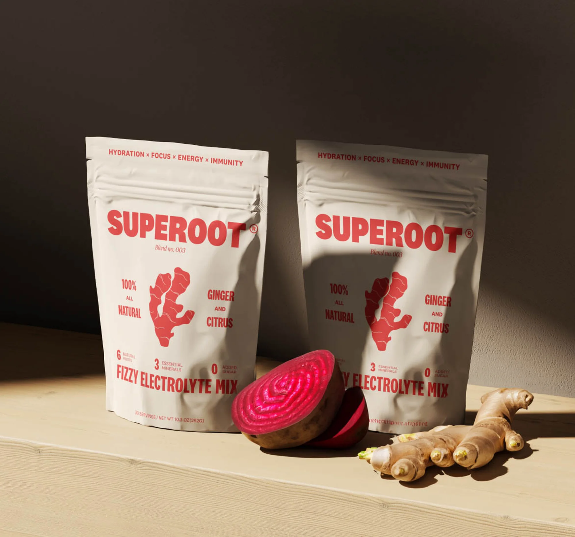 Two Superoot electrolyte mix pouches with ginger and beet slices on a wooden surface, showcasing natural ingredients and product presentation.