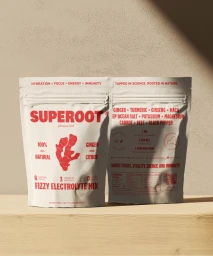Two Superoot electrolyte mix pouches displayed on a wooden surface against a textured neutral wall with natural light casting leaf shadows.