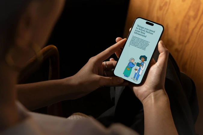 Woman holds smartphone displaying a cartoon illustration of doctor and patient, with healthcare info and a light teal background.