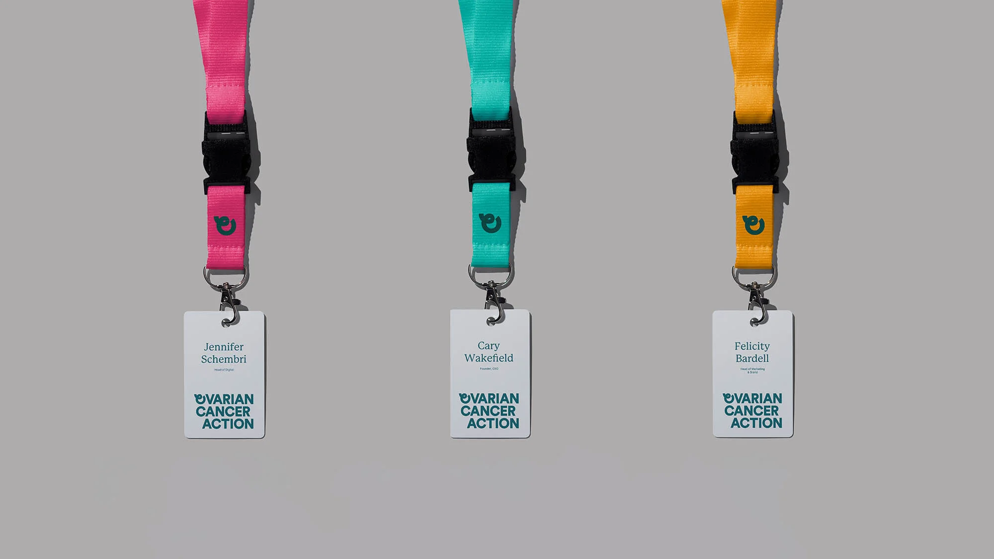 Three lanyards with name tags hang against a gray background. The lanyards are pink, teal and yellow, each displaying an organization logo.