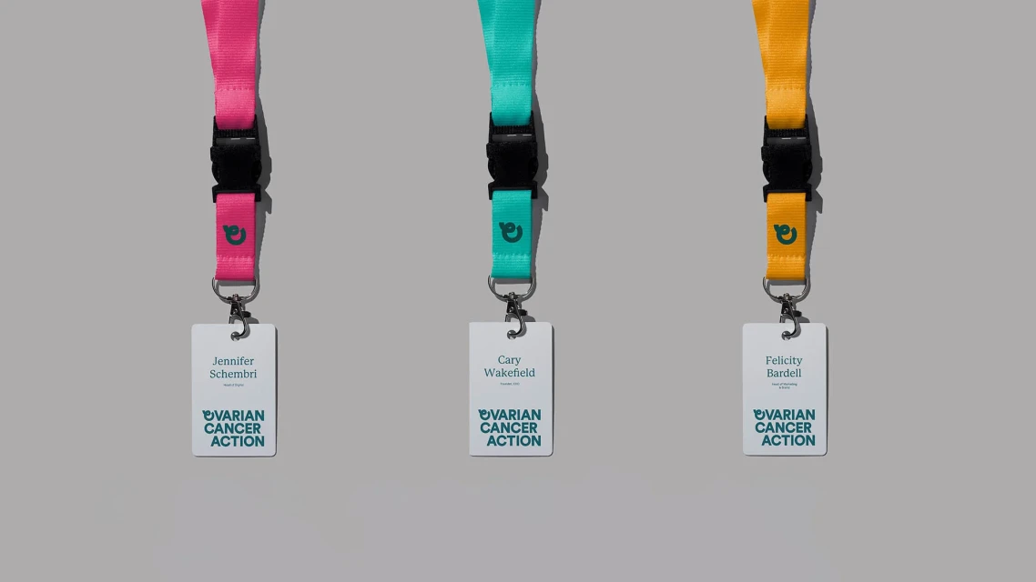 Three lanyards with name tags hang against a gray background. The lanyards are pink, teal and yellow, each displaying an organization logo.