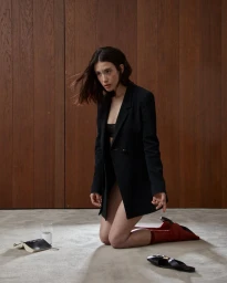 Woman wearing a black blazer and red socks kneeling on a concrete floor against a wood panel wall