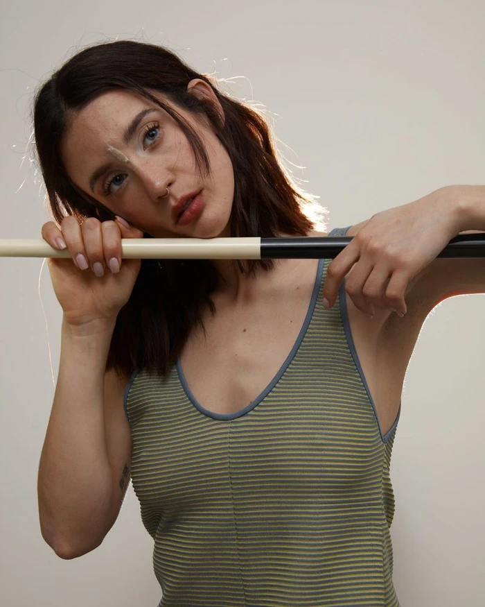 Portrait of María Pedraza leaning on a stick wearing a striped tank top against a seamless white studio background