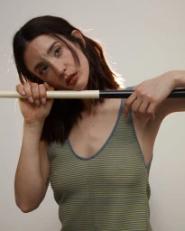 Portrait of María Pedraza leaning on a stick wearing a striped tank top against a seamless white studio background