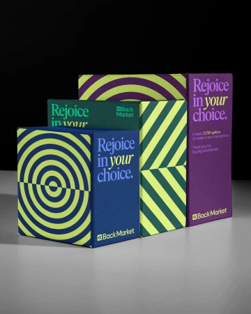 Back Market branded packaging in purple, green, and blue, arranged in a staggered row on a grey surface against a black background.
