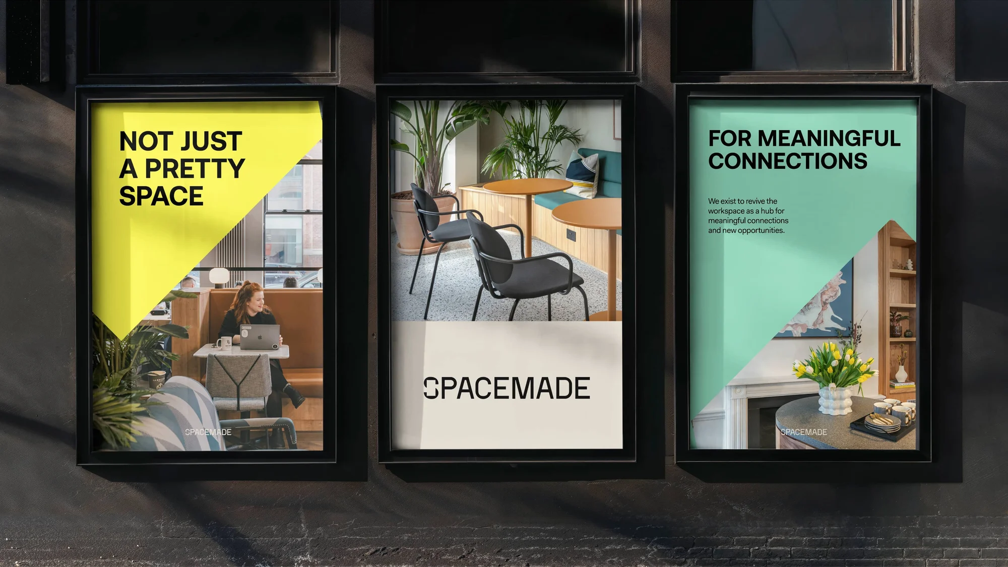 Three framed Spacemade advertisements hang on a dark wall featuring indoor scenes with furniture, plants, and an adult female with laptop.