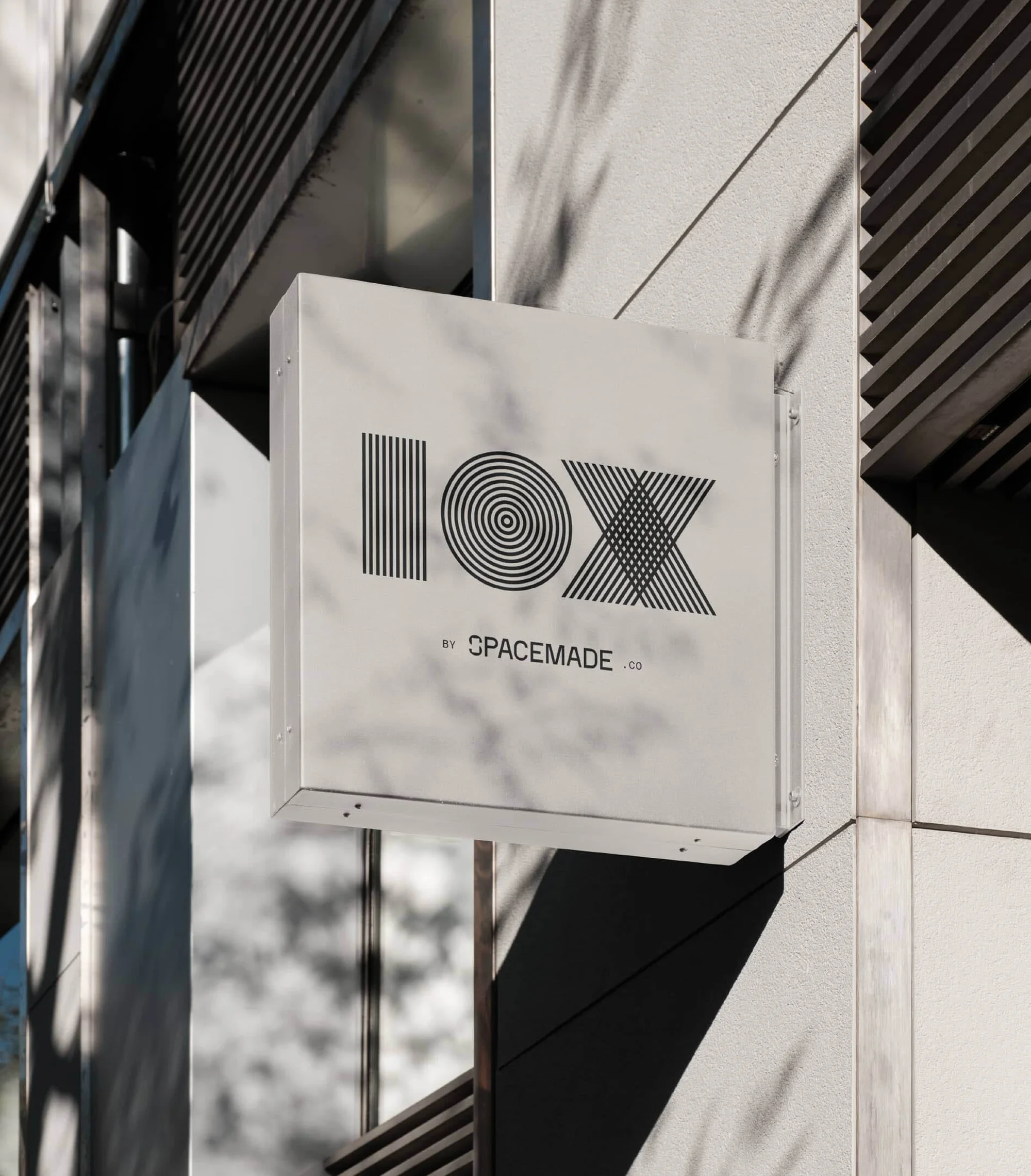 Exterior daytime shot of a minimalist white sign displaying the 'IOX' logo for Spacemade, mounted on the facade of a modern building.