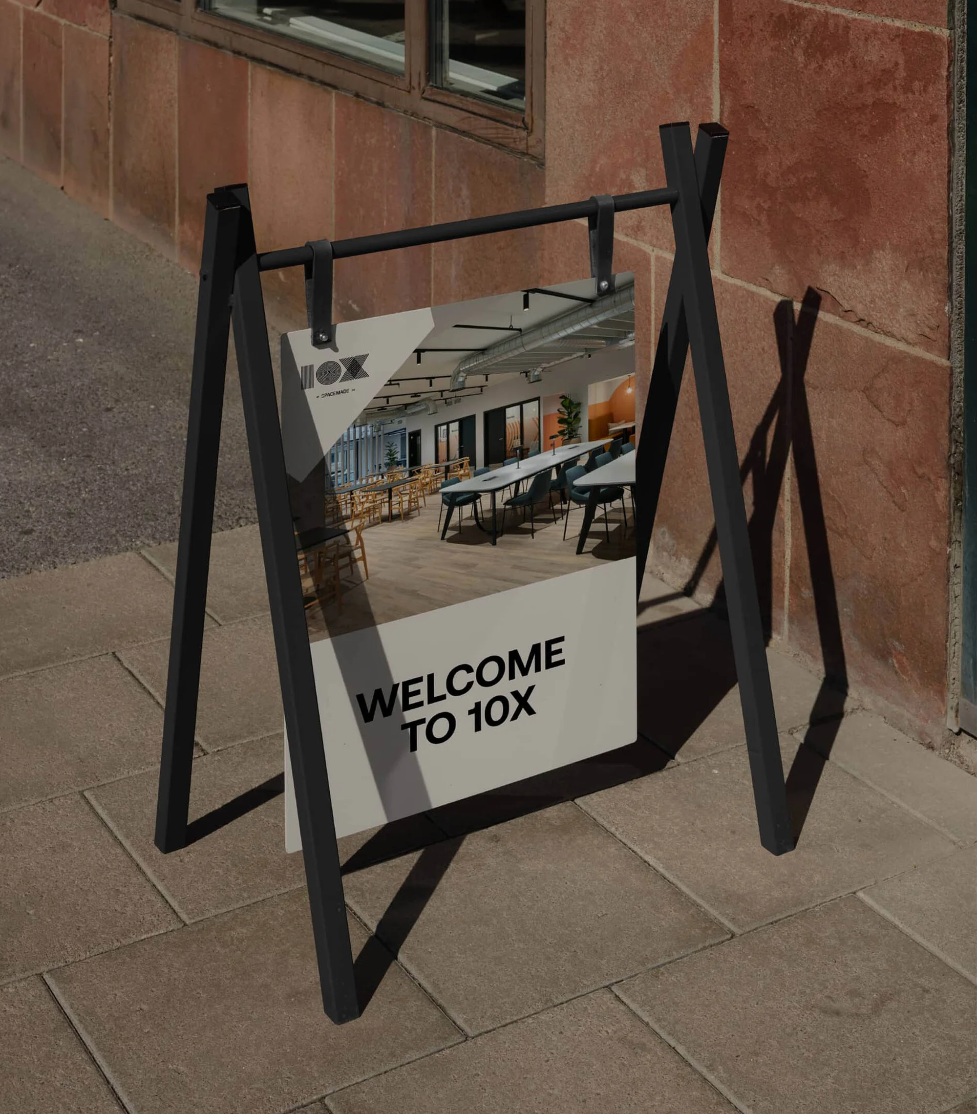 Signage display featuring the modern interior of 10X company, set outside on a stone path by a brown brick wall.