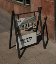 A-frame black metal sidewalk sign displaying brand graphics with text reading WELCOME TO 10X on a paved ground.