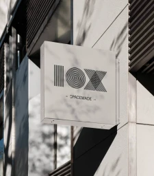 Exterior architectural sign featuring Spacemade brand identity on a modern building facade with sunlit shadow patterns.
