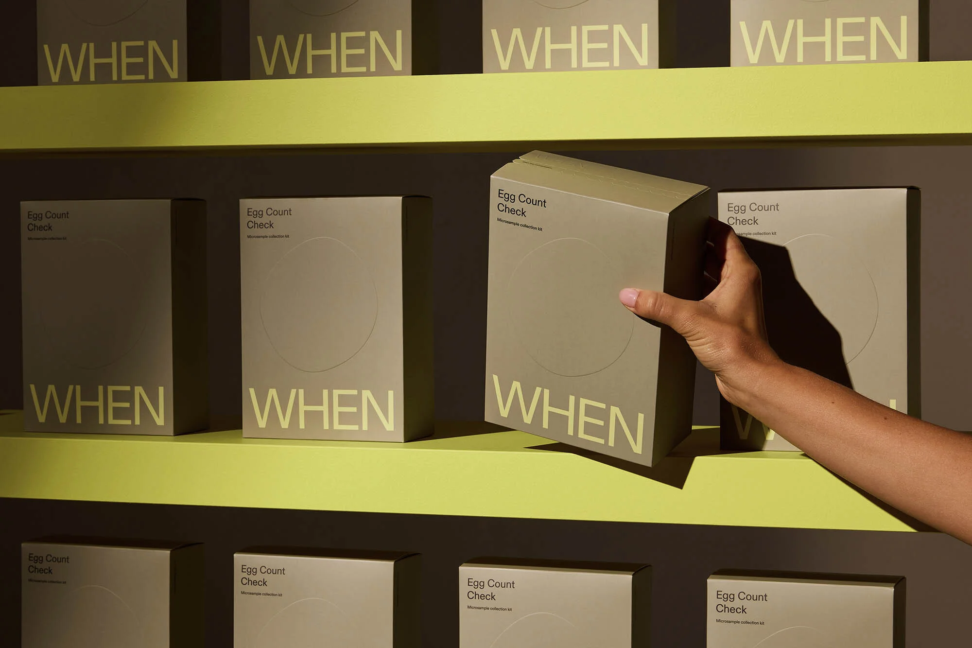 Boxes of egg count fertility tests are displayed on shelves, with a hand reaching for one. The packaging is beige with the word "WHEN".