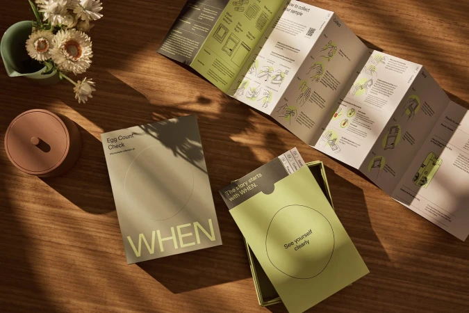 Top-down shot of a health test kit on a wood table, next to flowers in a vase. The kit box and instructions sit in direct sunlight.
