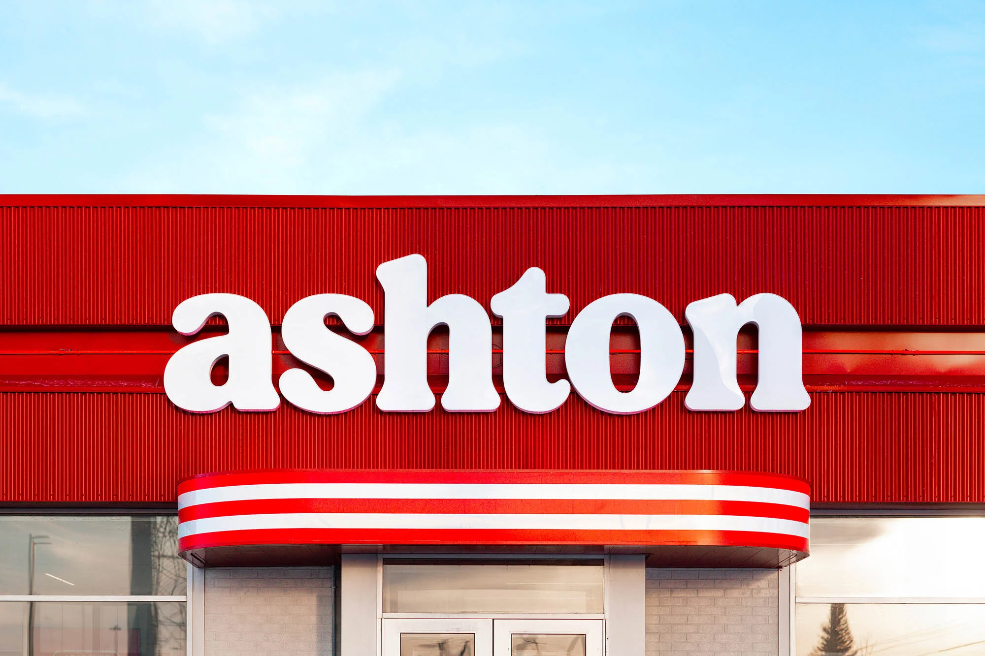Close-up of an Ashton restaurant exterior featuring a red facade, white lettering, and blue sky above. Building has a retro design.
